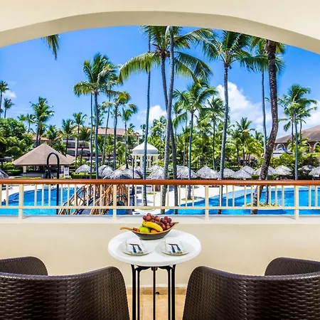 Majestic Colonial Punta Cana (Adults Only) Exterior photo This is a bright and inviting photo, likely taken from a hotel or resort balcony, offering a view of lush tropical scenery.

**Foreground:**
In the immediate foreground, there is a seating area featuring two dark brown, woven wicker chairs placed on 